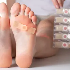 Plaster na stopie z widocznym nagniotkiem, obok opakowanie plastrów.