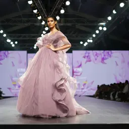 Modelka prezentuje suknię haute couture w kolorze pudrowego różu z falbanami i zdobieniami na wybiegu.